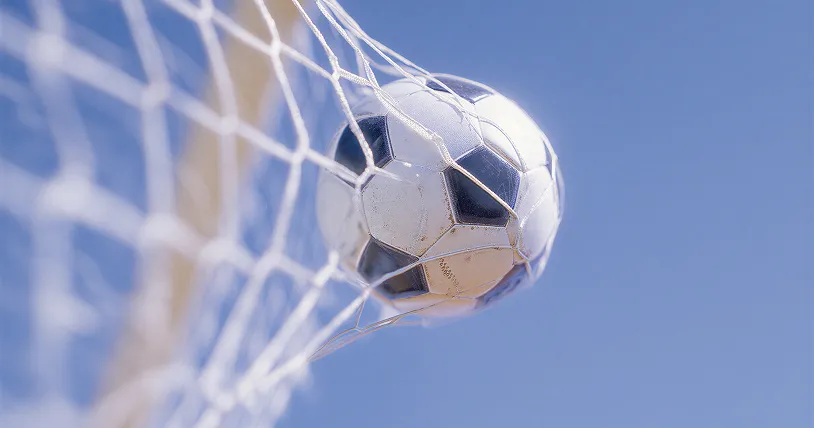 Black and white soccer ball caught in a white goal net against a clear blue sky.
