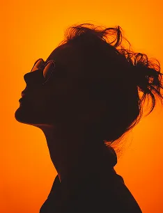 Silhouette of a woman with glasses and hair tied up against an orange background.